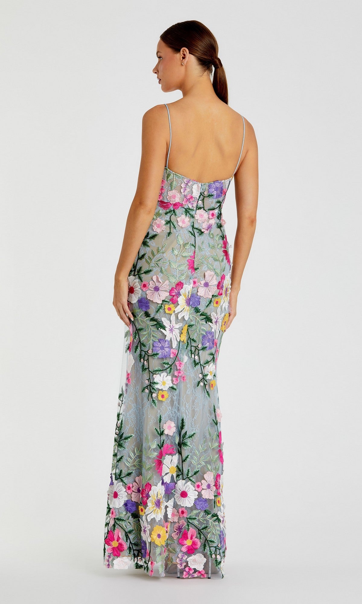 Woman facing away, wearing the Mac Duggal 68897 long formal dress—a sleeveless evening gown with colorful floral embroidery and thin straps—stands against a neutral background.